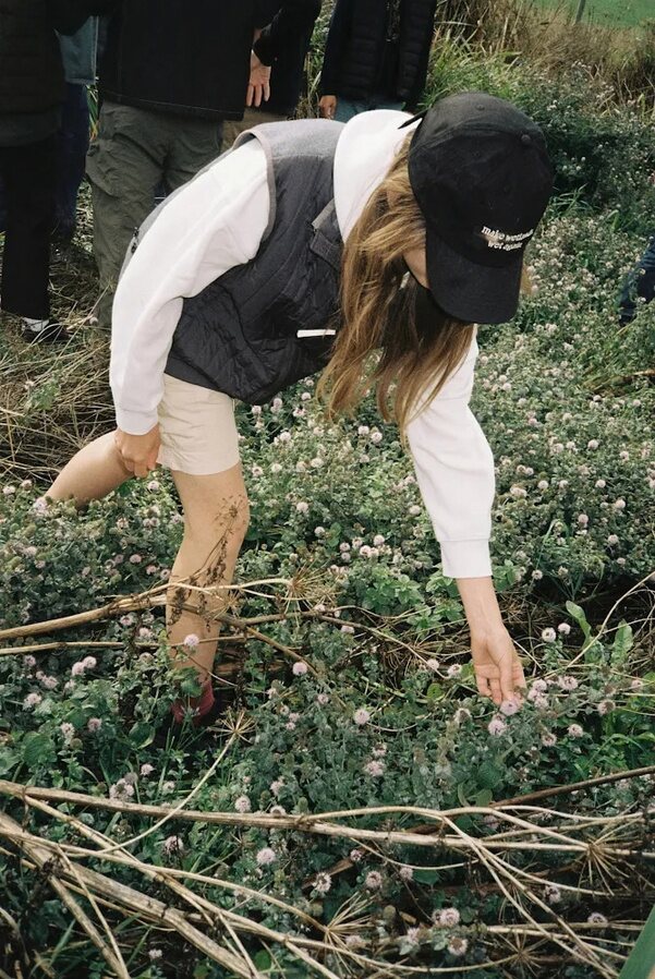 A woman in a Mallard gilet leaning into wetland plants